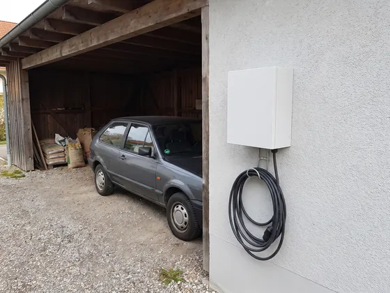 Weiße Wandladestation am Carport mit aufgehängtem Ladekabel